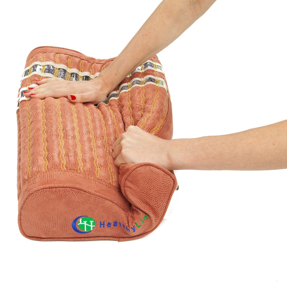 A person presses a textured, brown TAO-Mat® Pillow Soft InfraMat Pro® with both hands. The HealthyLine logo with a small blue and green globe icon is at the corner. This memory foam pillow features a wave-like design, perfect for neck support and promises ultimate comfort and relaxation.