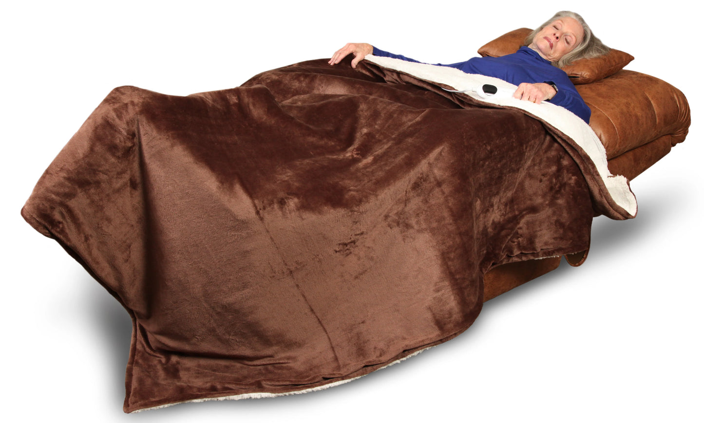 An older woman with gray hair relaxes on the Journey Health & Life Style Perfect Sleep Chair, covered by a large brown plush blanket. She wears a blue long-sleeve top and appears comfortable in the dual motor recliner.