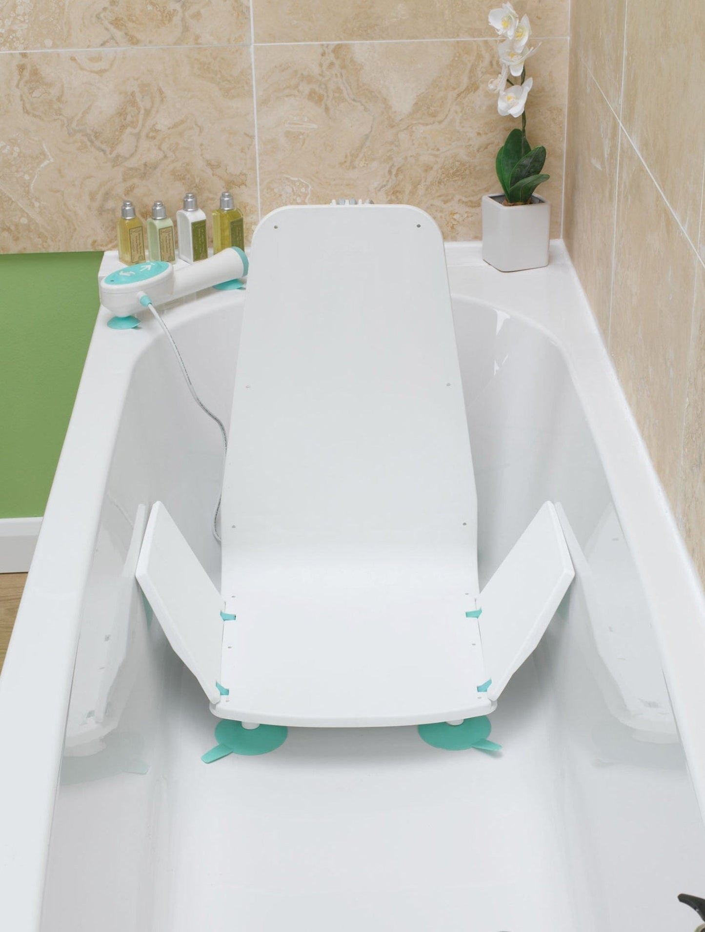 The Splash Bath Lift by Graham Field, a lightweight and budget-friendly adjustable bath chair, is installed in a tub with beige tiled surroundings. It includes a reclining backrest and arm supports, while toiletries rest on the edge and an orchid adorns the green wall in the background.