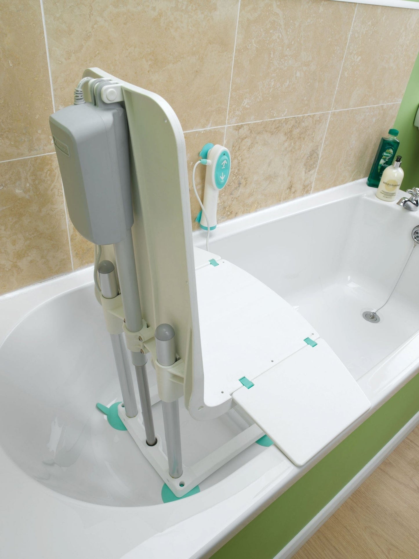 The Splash Bath Lift by Graham Field, featuring a foldable seat and attached control device, is installed in a white tub. Beige tiles surround it, while green and white toiletries sit on the edge for convenience.