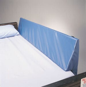 A bed with a white sheet and light blue pillow features a padded blue vinyl protector by Skil-Care Corporation, perfect for safety and comfort. The Bed Rail Wedge with Pad adds extra entrapment protection against the light gray wall, ideal for seizure patients.