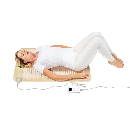 A person dressed in white is lying comfortably on the SOFT Mat Medium 4024 InfraMat Pro® by HealthyLine, a rectangular heated gemstone mat equipped with a cord and digital control panel. With knees bent and eyes closed, they are enjoying the calming warmth of the amethyst beneath them.