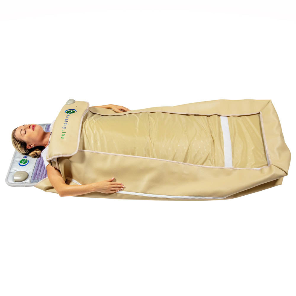 A woman relaxes on her back inside the HealthyLine Platinum 360 Wrap Set Full 7224 - Photon Advanced PEMF, a large beige thermal sauna blanket with a control panel at the headrest for a soothing full-body experience.