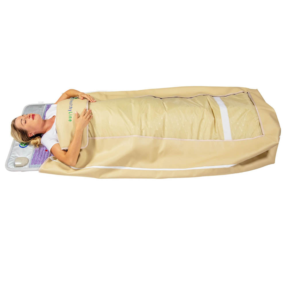 A person lies on a 360 Wrap Set™ Platinum & SOFT Full Pro PLUS 7428 - Photon Advanced PEMF InfraMat Pro® by HealthyLine, wrapped in a beige thermal blanket. With advanced gemstone technology controls at their side, they appear relaxed and soothed, enjoying the full-body experience.