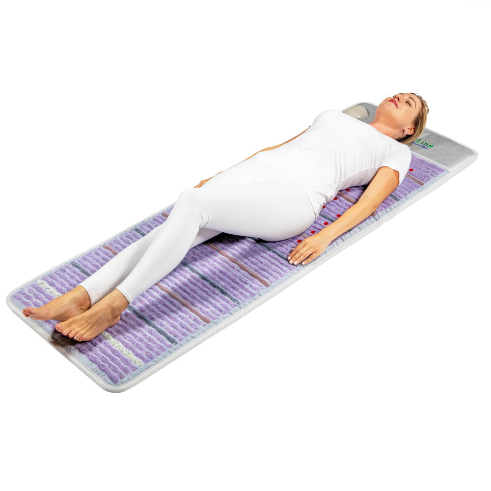 Dressed in white, an individual is reclining on the Platinum Mat™ Full 7224 Firm - Photon Advanced PEMF InfraMat Pro® by HealthyLine. The mat features a purple and white pattern with a small pillow supporting their head. Enhanced with gemstone heat therapy, it offers maximum relaxation against a solid white background.