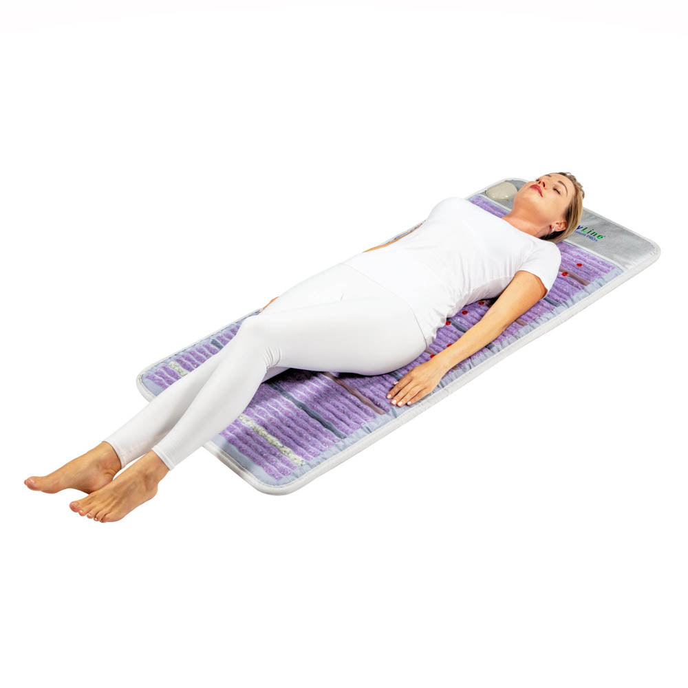 A woman in white lies on her back on a HealthyLine Platinum Mat Full Short 6024 with 30 Photon LED and advanced PEMF, featuring a purple textured surface, arms by her sides and legs extended.