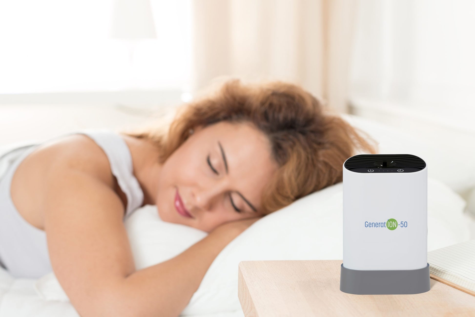 A woman peacefully sleeps on a bed with white sheets. In the foreground, a Generation-50 Air Purifying Device by HealthyLine purifies the air, sitting on a wooden nightstand. This negative ion generator operates without ozone. A lamp and curtains are blurred in the background.