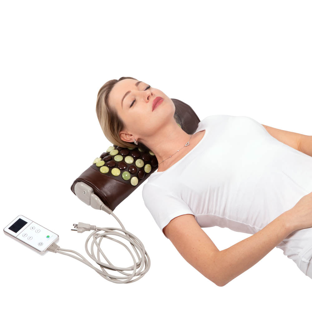 A person with closed eyes relaxes on a Pebble JT Bolster Firm InfraMat Pro® by HealthyLine, featuring a pillow embedded with round jade and tourmaline gemstones. Connected to a small electronic control device, this setup enhances their relaxation while wearing a white top.
