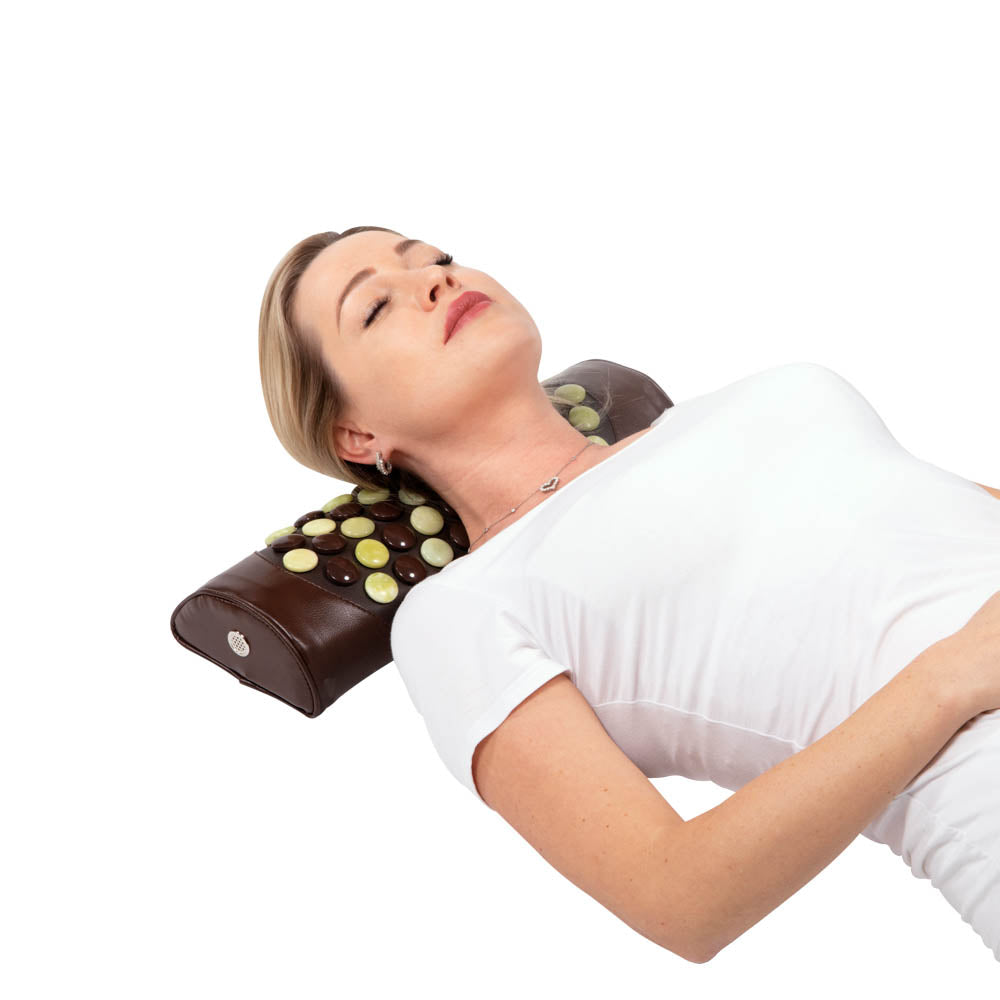 A person in a white shirt lies down with the Pebble JT Bolster Firm InfraMat Pro® by HealthyLine, featuring embedded round stones. The jade and tourmaline gemstones emit far-infrared rays, which contribute to the person's relaxed appearance.