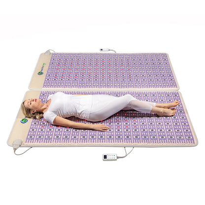 A person dressed in white lies on the HealthyLine TAJ-Mat™ King 8076 Firm, a large rectangular mat with a geometric pattern, spread out on a flat surface. Nearby, a remote control suggests the soothing benefits of hot gemstone therapy for profound relaxation.