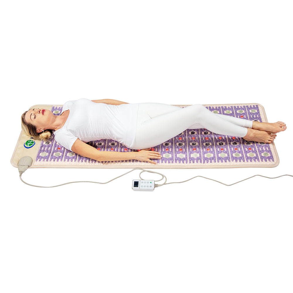Relaxing on the elegant TAJ-Mat™ Full 7224 Firm by HealthyLine, someone in white peacefully lies back with closed eyes, savoring the soothing wellness benefits from its intricate purple and beige patterns against a light surface.