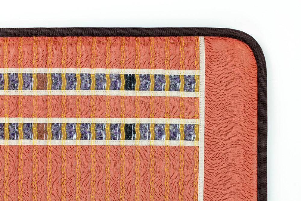The TAO-Mat® Full 7224 Firm from HealthyLine showcases a geometric pattern accented with crushed gemstones. It features a rust-red base with vertical and horizontal stripes in blue, brown, and yellow tones, all bordered in black.