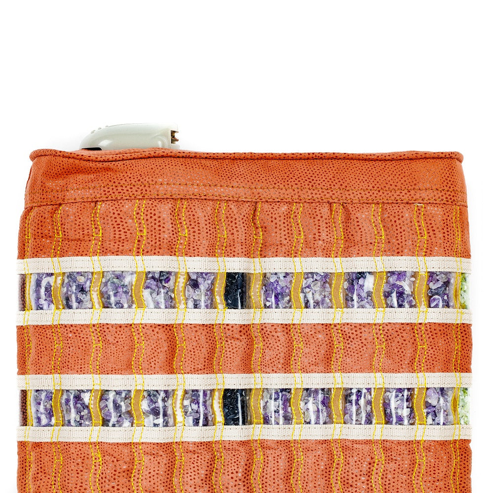The TAO mat Pillow with Heat from HealthLine showcases a textured orange fabric with horizontal white stripes interlaced with purple and yellow patterns, reminiscent of heated gemstones. A discreet white button at the top suggests hidden features beneath the vibrant surface.