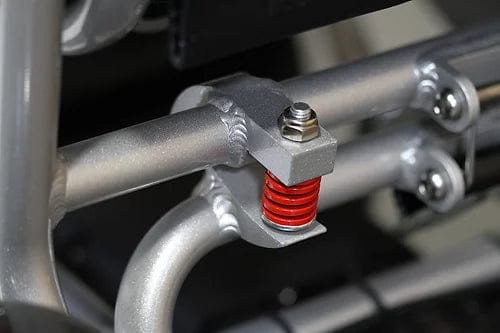 A close-up of the EW-M45 Portable Power Wheelchair by E-Wheels showcases a mechanical part with a metal bolt and a prominent red coil spring mounted on two silver rods, indicative of its suspension or damper mechanism—a design frequently incorporated into lightweight folding wheelchairs to ensure enhanced durability.