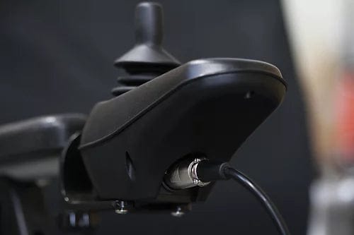 Close-up of a black joystick with a cable attached, set against a blurred dark background. The joystick, reminiscent of those used in the EW-M45 Portable Power Wheelchair by E-Wheels, features a smooth surface and simple design, making it ideal for precise control and navigation.