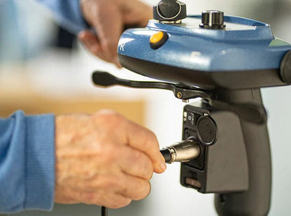 A person connects a cable to a blue handheld device with buttons, dials, and a lever—suggesting technical work on the So Lite Scooter by Journey Health & Life Style, known for its lightweight mobility and advanced safety features.