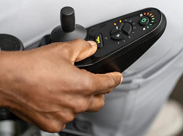 A hand expertly operates the Zoomer by Journey Health & Lifestyle's one-handed joystick control panel, featuring vibrant buttons, indicators, a speed dial, and a power button for smooth navigation.