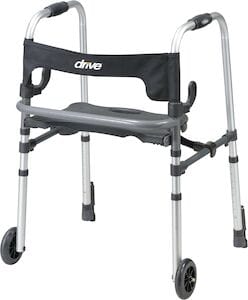 The Walker Clever Lite LS by Drive Medical is a silver rollator with front wheels, rear rubber stoppers, and a black fabric backrest. It includes a gray foldable seat labeled "drive" and features a dual-lever folding system for portability and push-down brakes for safety.