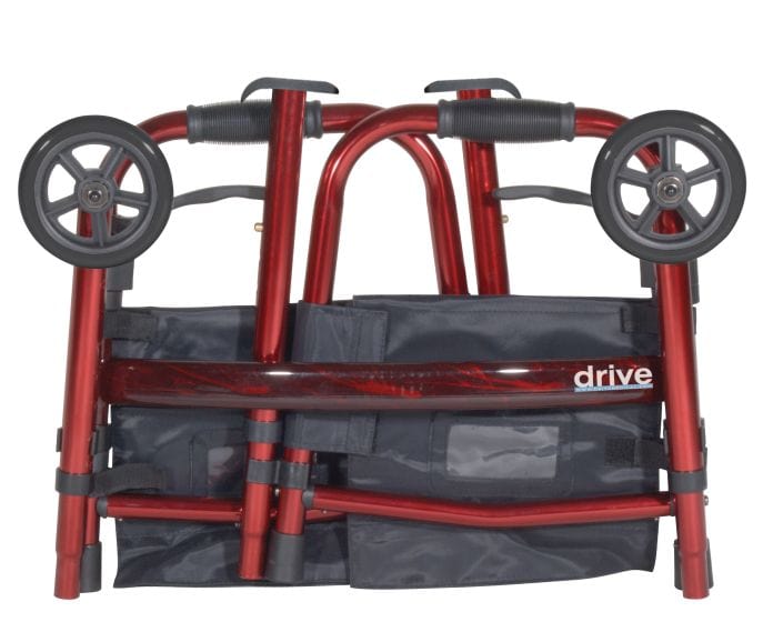 A travel walker with folding legs from Drive Medical is displayed in red, featuring black handles and two wheels. It includes a fabric storage pouch that prominently showcases the "Drive Medical" brand name in white on the side, ensuring convenient transportability.